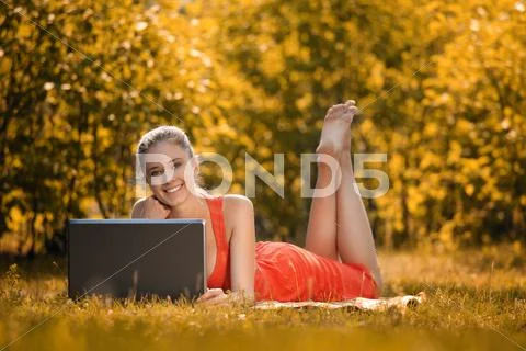 Young Woman With Laptop In The Park On Grass, In Autumn