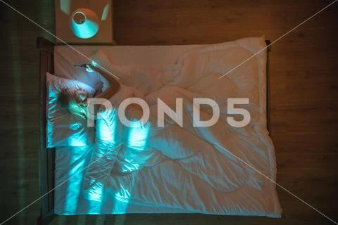 The young woman lay on the bed and phone. Evening night time. View from above Stock Photos
