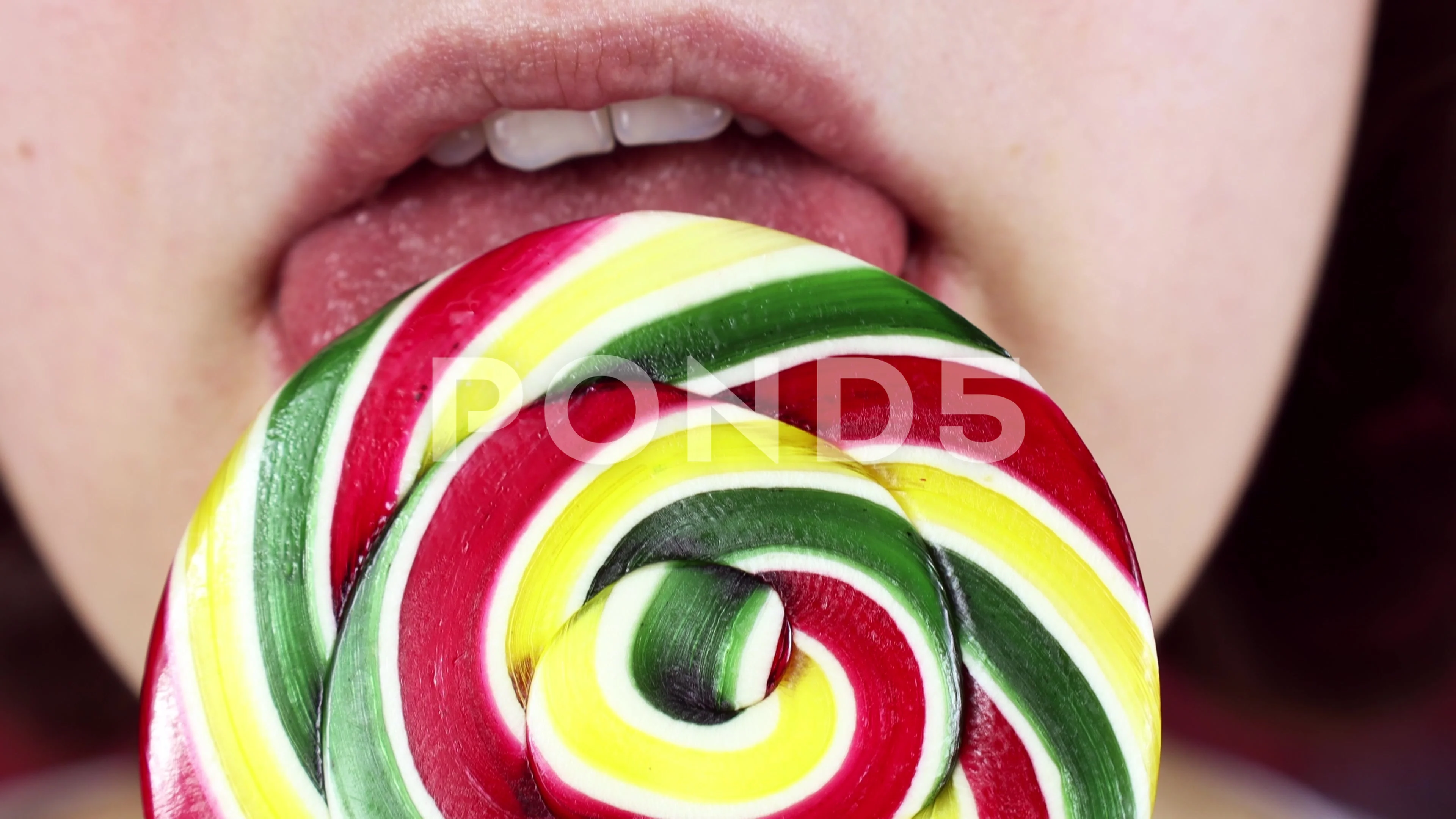 Young woman licking a bright colorful lollipop candy with a tongue close up