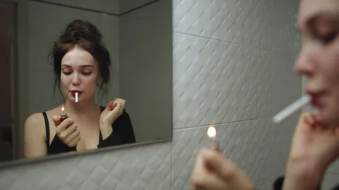 Young woman lighting a cigarette while looking at herself in the mirror Stock Footage 314905520