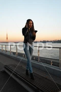 Young woman listens to music in closed headphones through her phone wearing a Stock Photos
