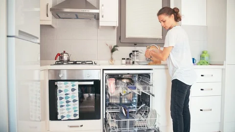 Young woman loading the dishwashing machine Stock Footage 129489755