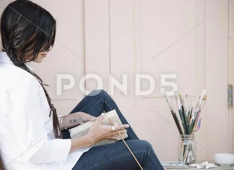 Young woman with long brown hair, holding a sketch book and paint brush. Stock Photos