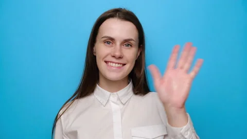 Young woman looking at camera with charming smile waving greeting with hand Stock Footage 133458886