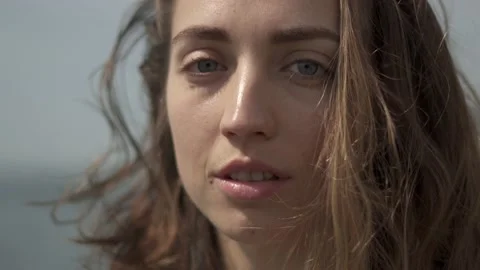 Young woman looking at camera while standing at seaside during sunny day Stock Footage 132049363