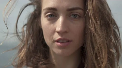 Young woman looking at camera while standing at seaside during sunny day Stock Footage 132050103