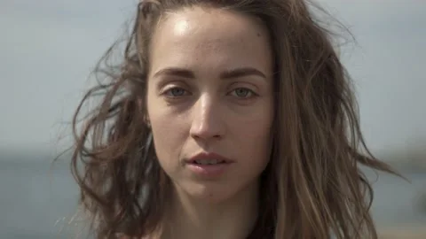 Young woman looking at camera while standing at seaside during sunny day Stock Footage 132050936