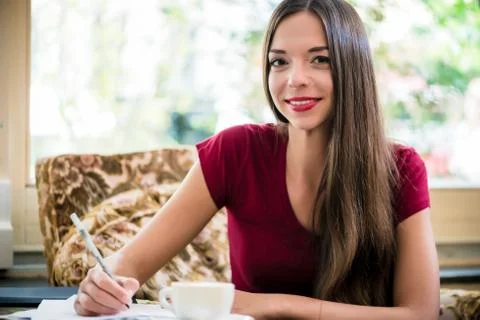Young woman looking at camera while writing indoors Stock Photos