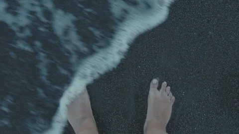 Young woman looking down at bare feet on black sand in ocean water Stock Footage 306863792