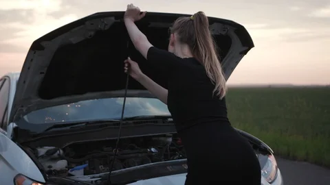 Young woman looking at engine of breakdown car at the field closes the hood of Stock Footage 112747732