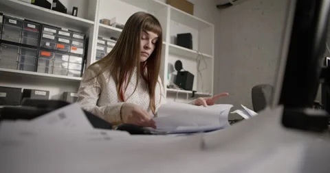 A young woman is looking for the right document on a table littered with papers. Vidéo 172344409