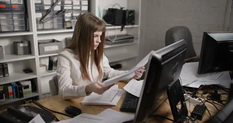 A young woman is looking for the right document on a table littered with paper. Stockbeeldmateriaal 172344686