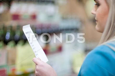 Young Woman Looking At Shopping List In Supermarket
