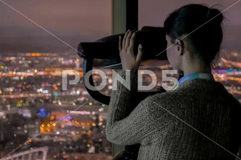 Young woman looking through tourist telescope and exploring night cityscape Stock Photos