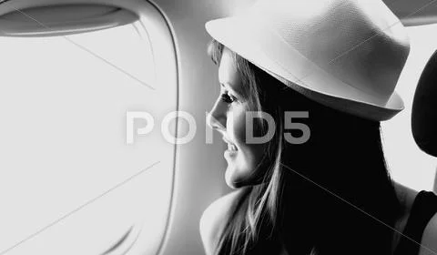 Young woman is looking through a window in the aircraft Stock Photos