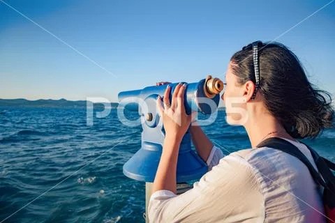 Young woman looks in a telescope or binoculars by the sea. Stock Photos