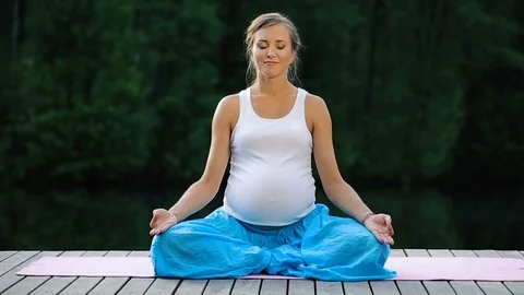 Young woman in the lotus position is practicing yoga in the forest next to the Stock Footage 71672227