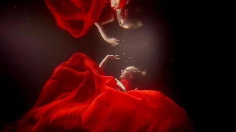 A young woman in a lush red dress swims under the water, she touches the Stock Footage