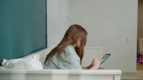 Young woman lying on bed studying on tablet, side profile shot in minimalist Stock Footage 333475764
