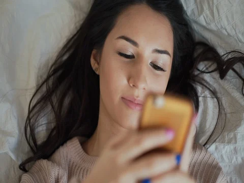 Young woman lying in bed using mobile phone and smiling Stock Footage 74588318