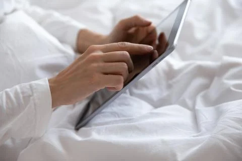 Young woman lying in bed, using computer digital tablet. Stock Photos