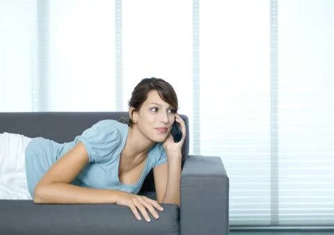 Young woman lying on couch, using cell phone Stock Photos