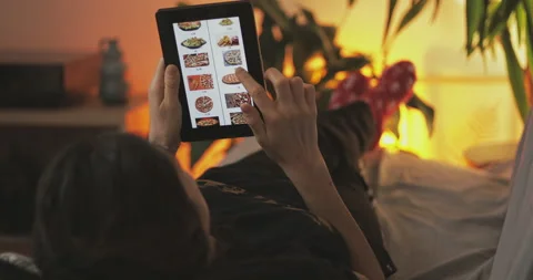 Young woman lying down in sofa at home and online order fast food fom home. Stock Footage 148390732