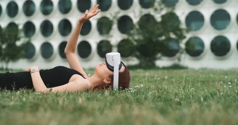 A young woman lying on the grass while trying virtual reality goggles Stock Footage 201117918