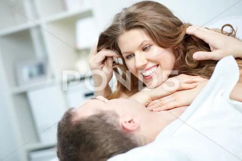 A young woman lying on her boyfriend in bed and the man stroking her hair Stock Photos