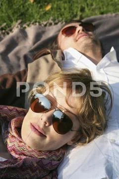 A young woman lying on her boyfriend's stomach outside Stock Photos