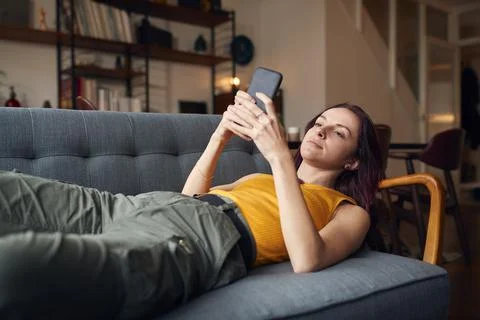 Young Woman Lying On Sofa At Home Looking At Mobile Phone Messages And Social Stock Photos