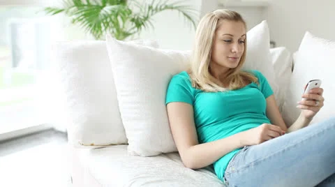 Young woman lying on sofa using mobile phone smiling and looking at camera Stock Footage 25911538