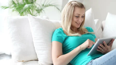 Young woman lying on sofa using touchpad smiling and laughing Stock Footage 25911541