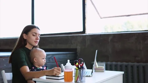 A young woman makes notes in a notebook, on her hands she holds a daughter Video stock 81219398