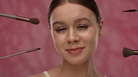 Young woman with makeup posing at camera in studio, cosmetic brushes popping Stock Footage 305775405