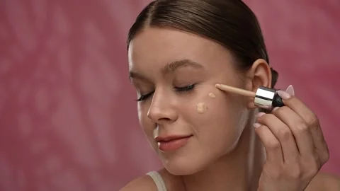 Young woman with makeup posing at camera in studio, smiling applying liquid tone Stock Footage 305775409