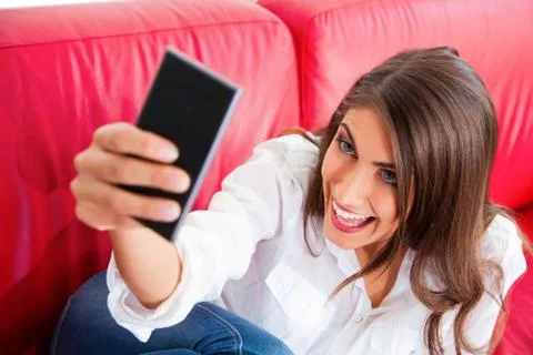 Young woman making face while taking selfie on sofa Stock Photos