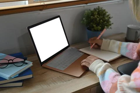 Young woman making notes on notebook and using computer laptop at home. Stock Photos