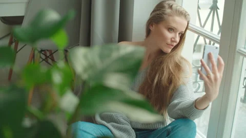 Young woman making selfie while sitting near a window at home. 動画素材 88829637