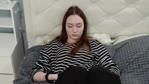 Young woman manipulating small object while sitting on bed Stock Footage 310766098