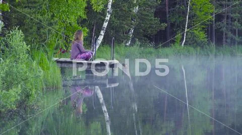 Young woman meditating on the shore of a lake Stock Photos