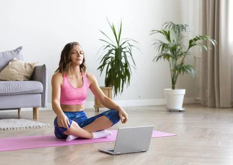A young woman is meditating using a tutorial on the internet. She sits with 写真素材