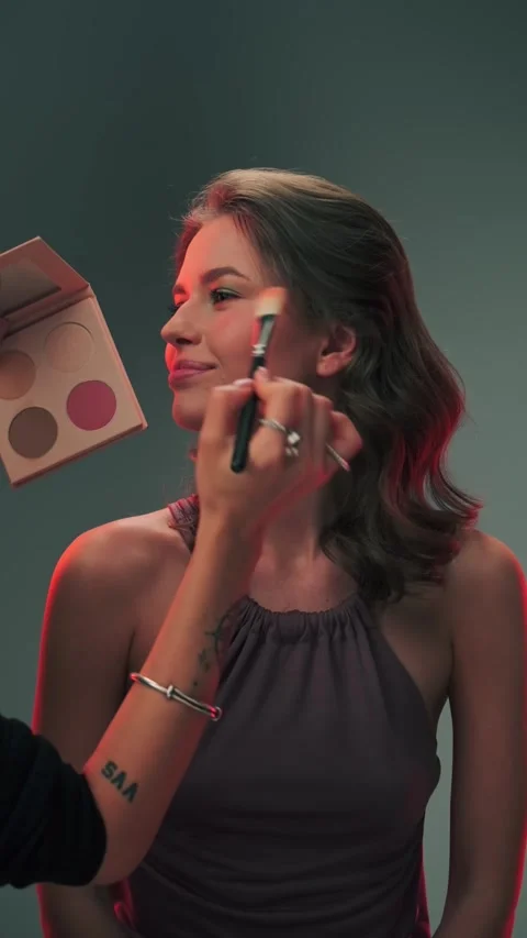 Young woman model in studio for shooting. The master applies makeup to her face. Stock Footage 340403168
