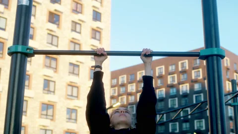 Young woman in morning practices pull-ups on bar in black hoodie with pigtail Stock Footage 202290153