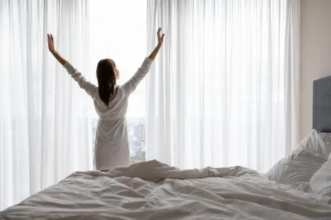 Young woman in night gown stretching muscles near window. Stock Photos