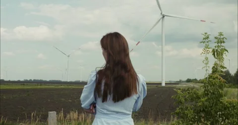 Young woman observing rotating wind turbines in a field Stock Footage 306907436