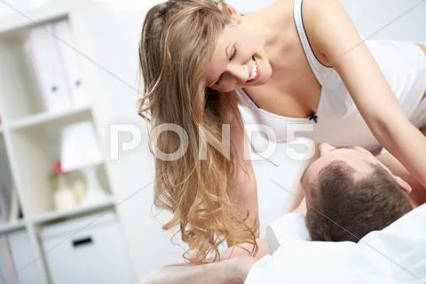 A young woman over her husband in bed looking at him and smiling Stock Photos