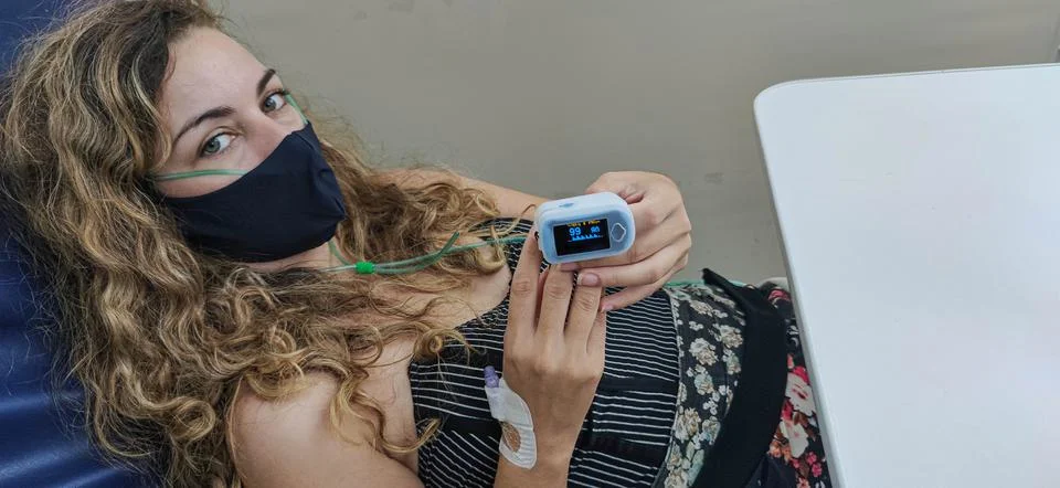 Young woman with oximeter on her finger receiving treatment against Covid-19  Stock Photos