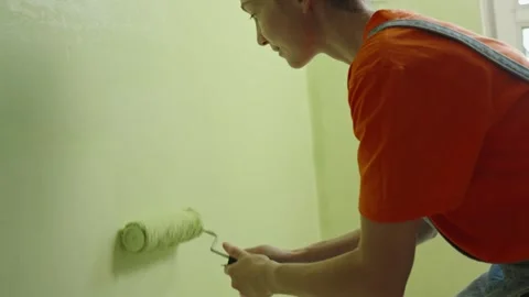 A young woman painter paints the wall green with a roller Stock Footage 279399341