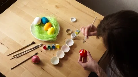A young Woman Paints Easter Egg with a Brush on the background of Wooden Table Stock Footage 61743497